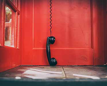 telephone receiver hanging touching the floor in a red call telephone booth. the concept of technological progress and the development of communication. Hanging up