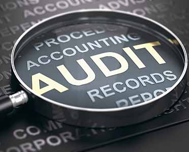 Financial Auditing Concept. Magnifying glass with focus on the word audit written in golden letters and other accounting words over black background. 3D illustration.